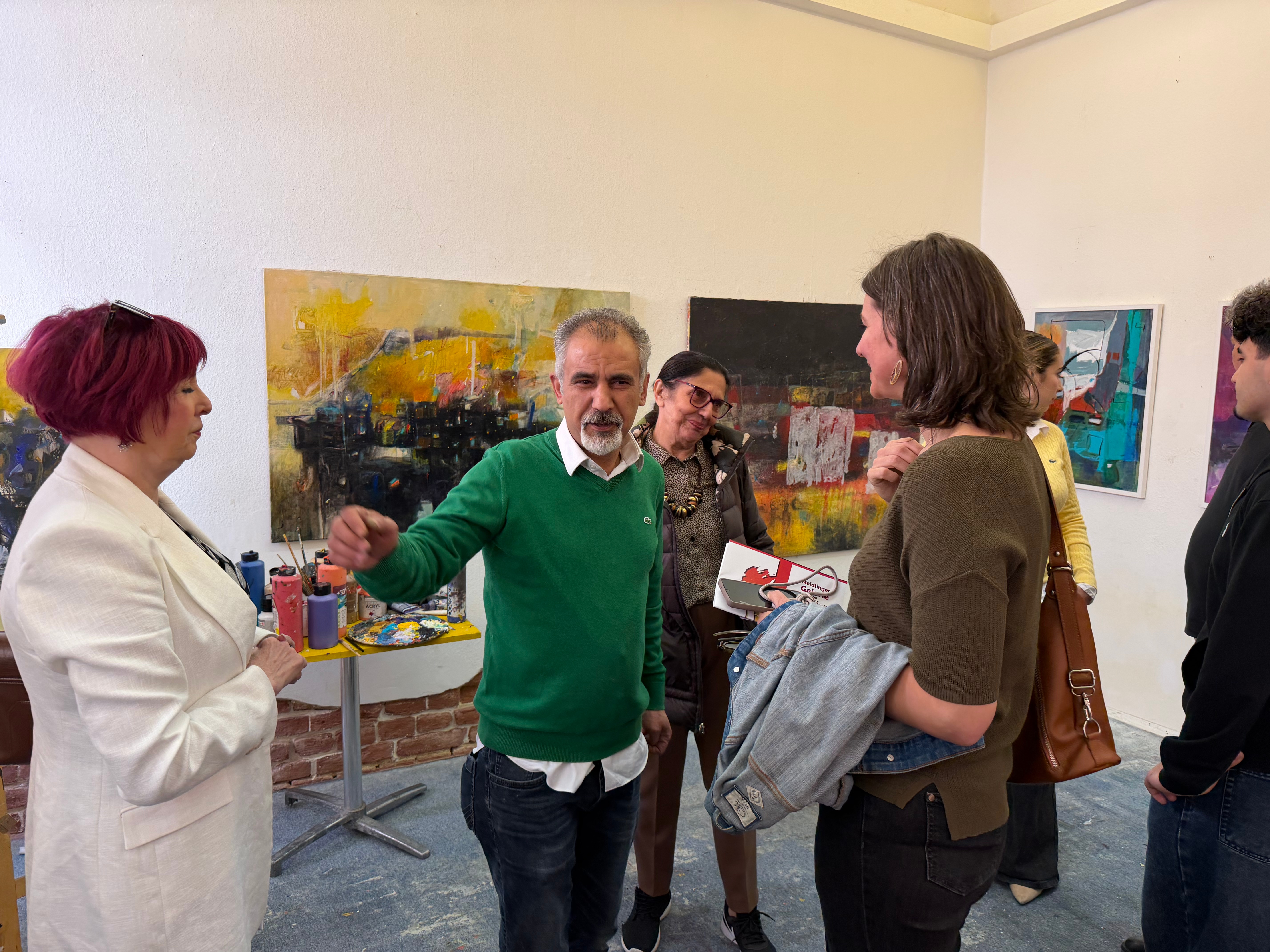 مجموعة من الأشخاص يتحدثون في استوديو فني، مع لوحات تجريدية ملونة في الخلفية.