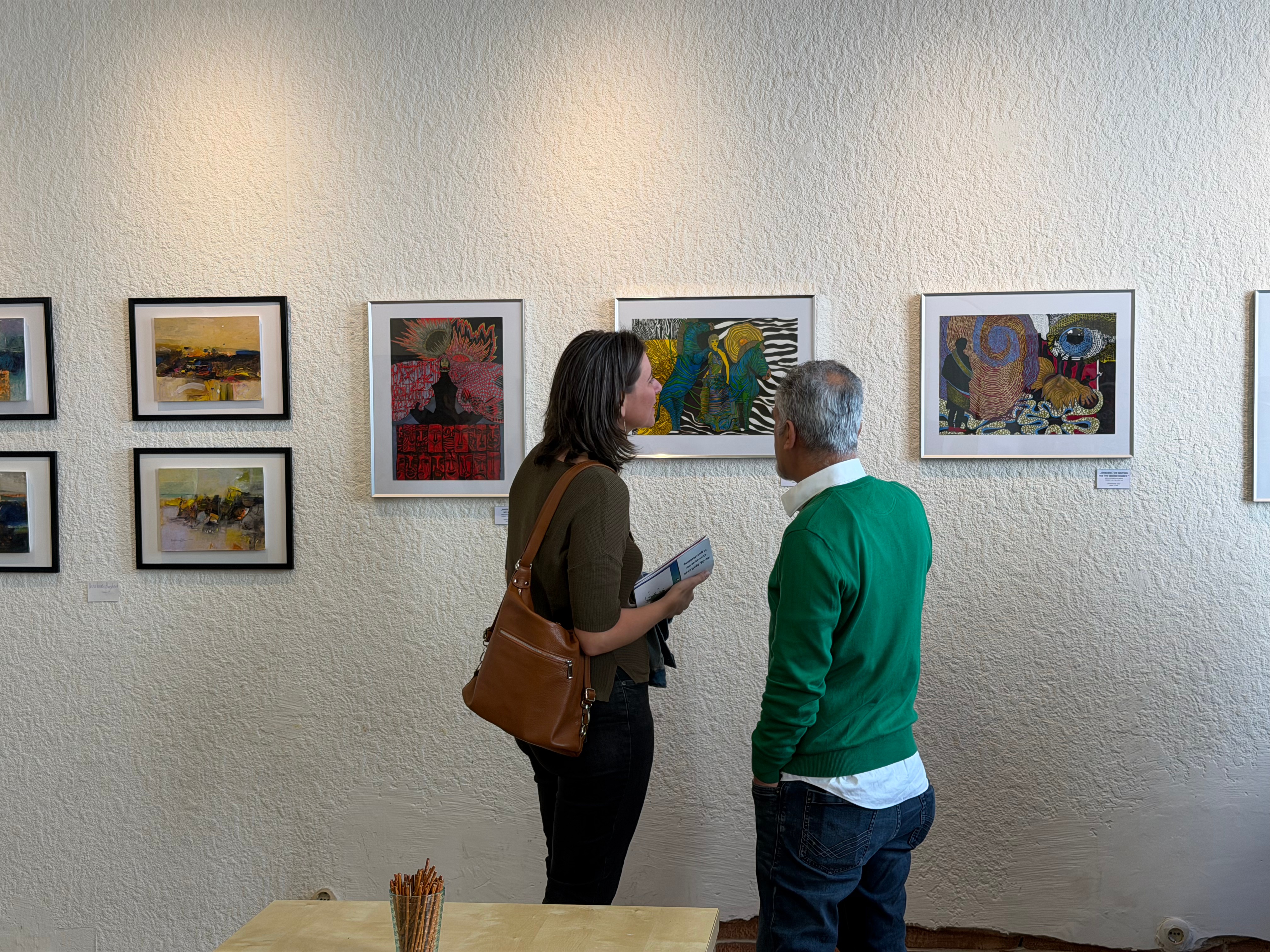 امرأة ورجل يتحدثان معًا أمام جدار مغطى باللوحات الفنية في معرض.