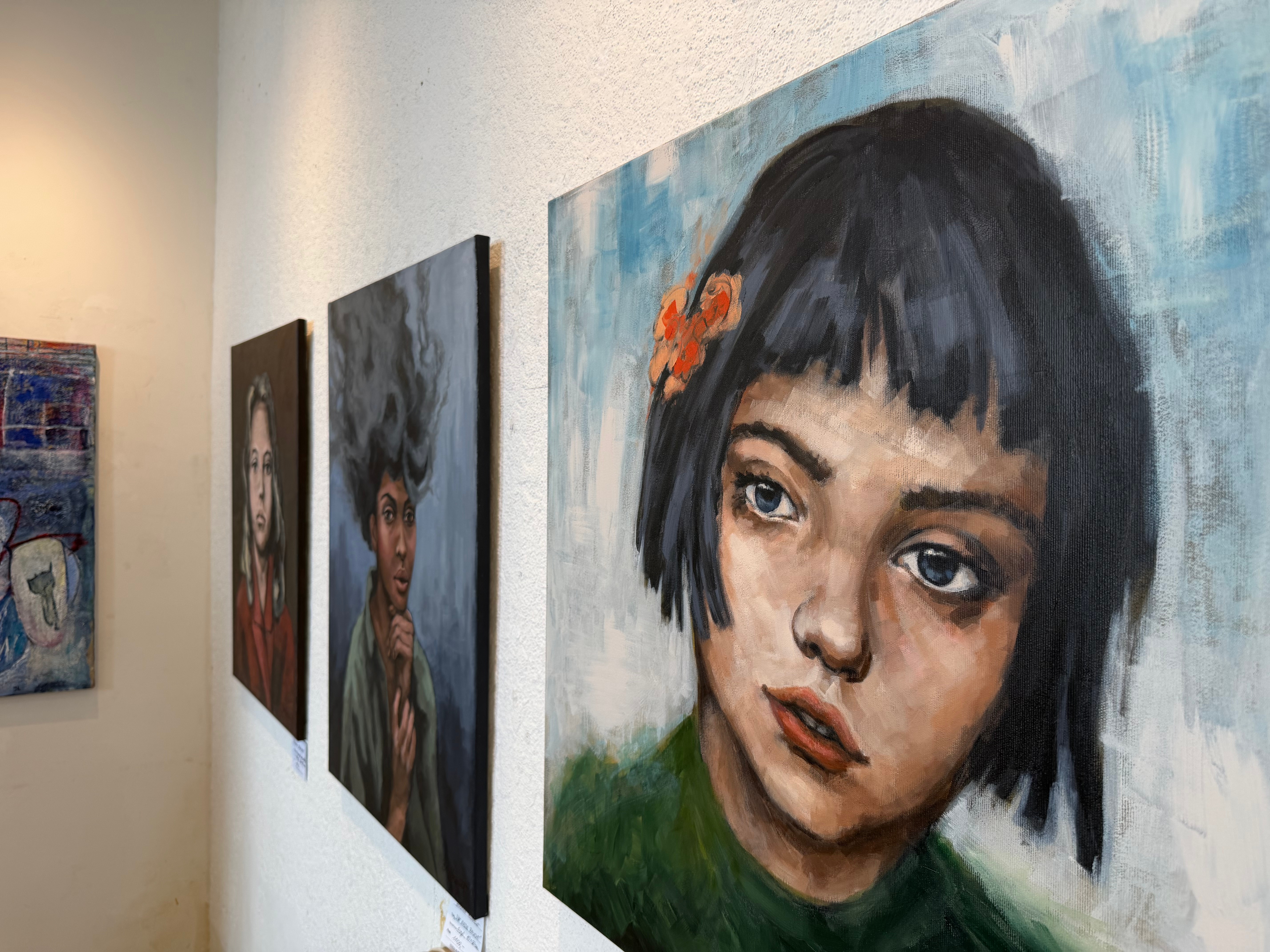 لوحة فنية تُظهر وجه فتاة ذات شعر قصير داكن وتضع زهرة برتقالية في شعرها، مع خلفية زرقاء.