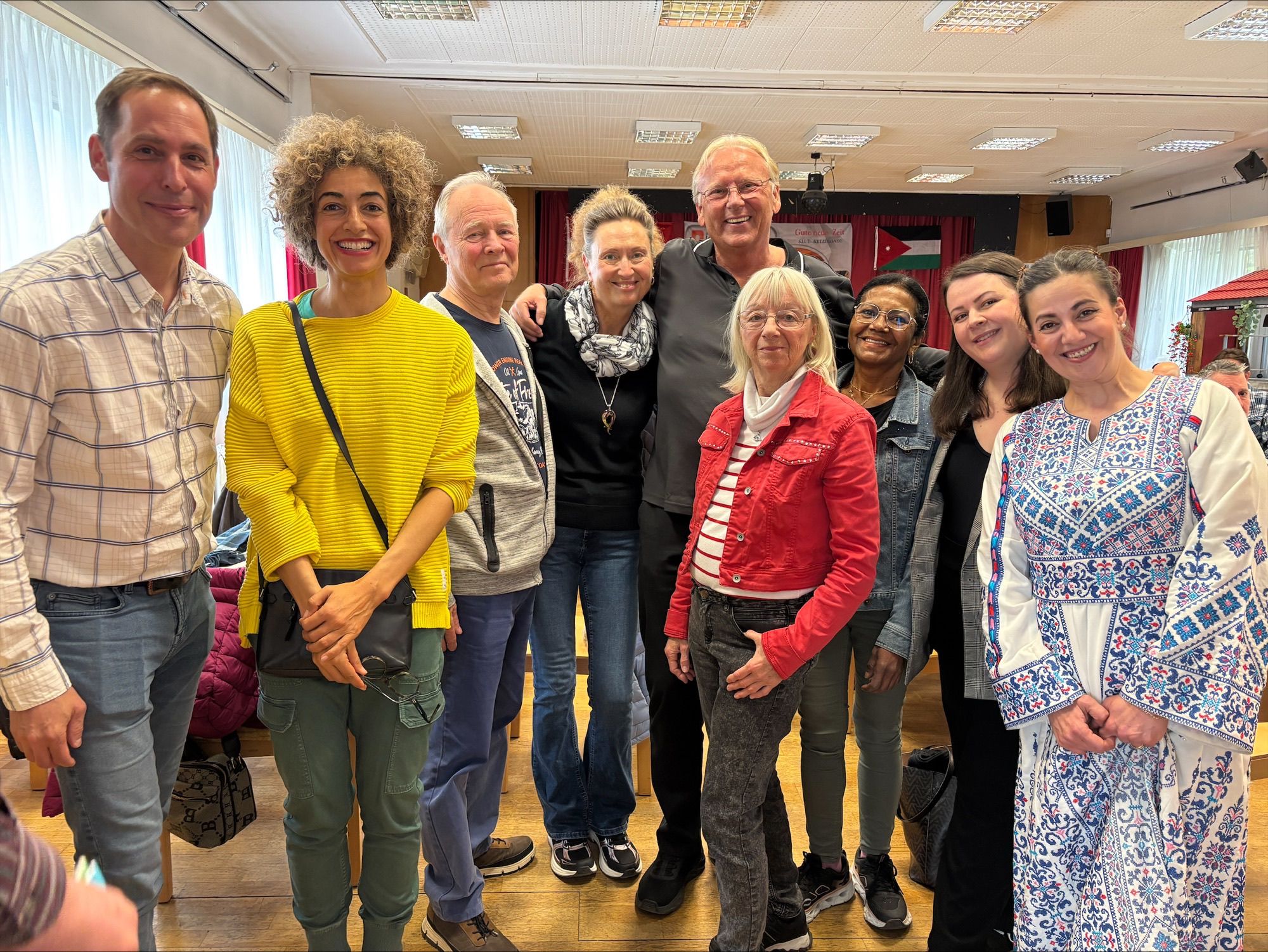 مجموعة من عشرة أشخاص يقفون معًا في غرفة مضاءة جيدًا، يرتدون ملابس ملونة ومتنوعة، مبتسمين أمام الكاميرا.