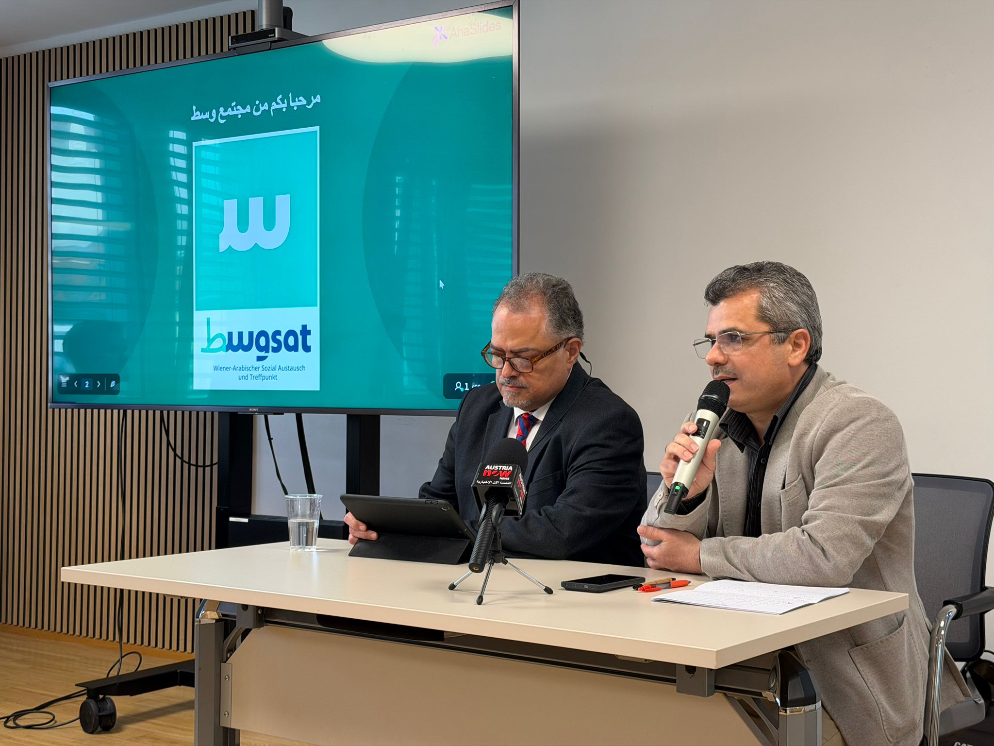 حدث يتضمن شخصين يتحدثان أمام شاشة تعرض شعار منظمة bwtagsat.