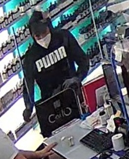 شخص يرتدي سترة سوداء تحمل شعار بومة داخل متجر، ويقوم بعملية سحب في اتجاه جهاز الكمبيوتر.